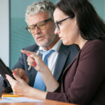 Two business professionals analyzing data on a tablet during a strategy meeting about regulatory reforms in financial institutions.