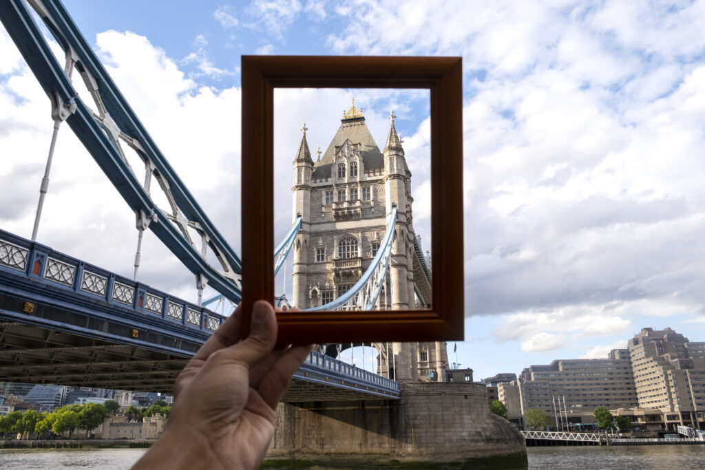 A hand holding a picture frame capturing the Tower Bridge in London, symbolizing the contrast between transparency and secrecy often associated with tax havens.